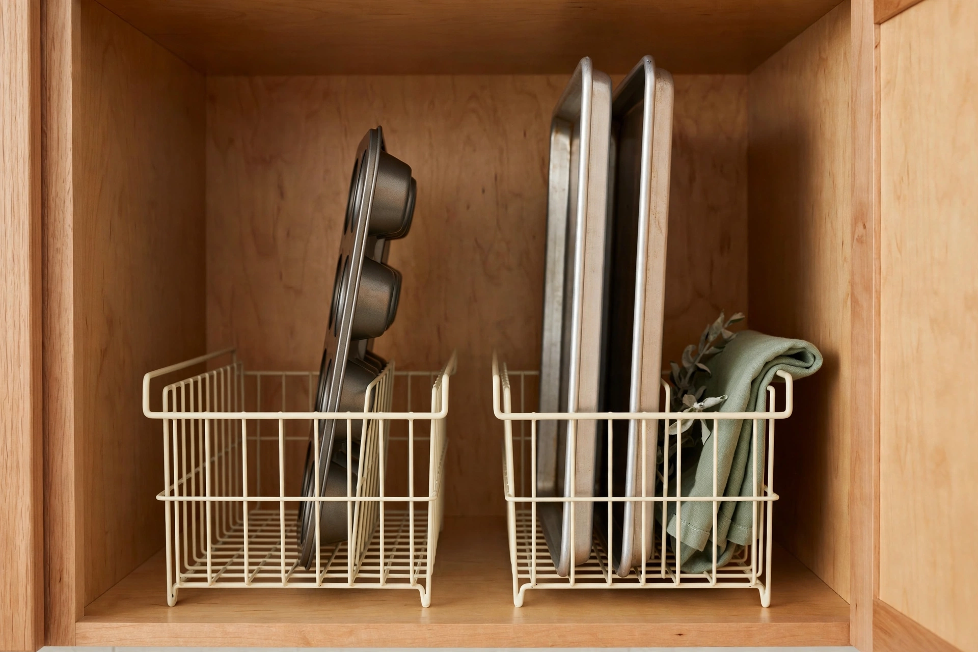 Wire file holders inside a kitchen cabinet organizing a muffin tin and sheet pans standing upright